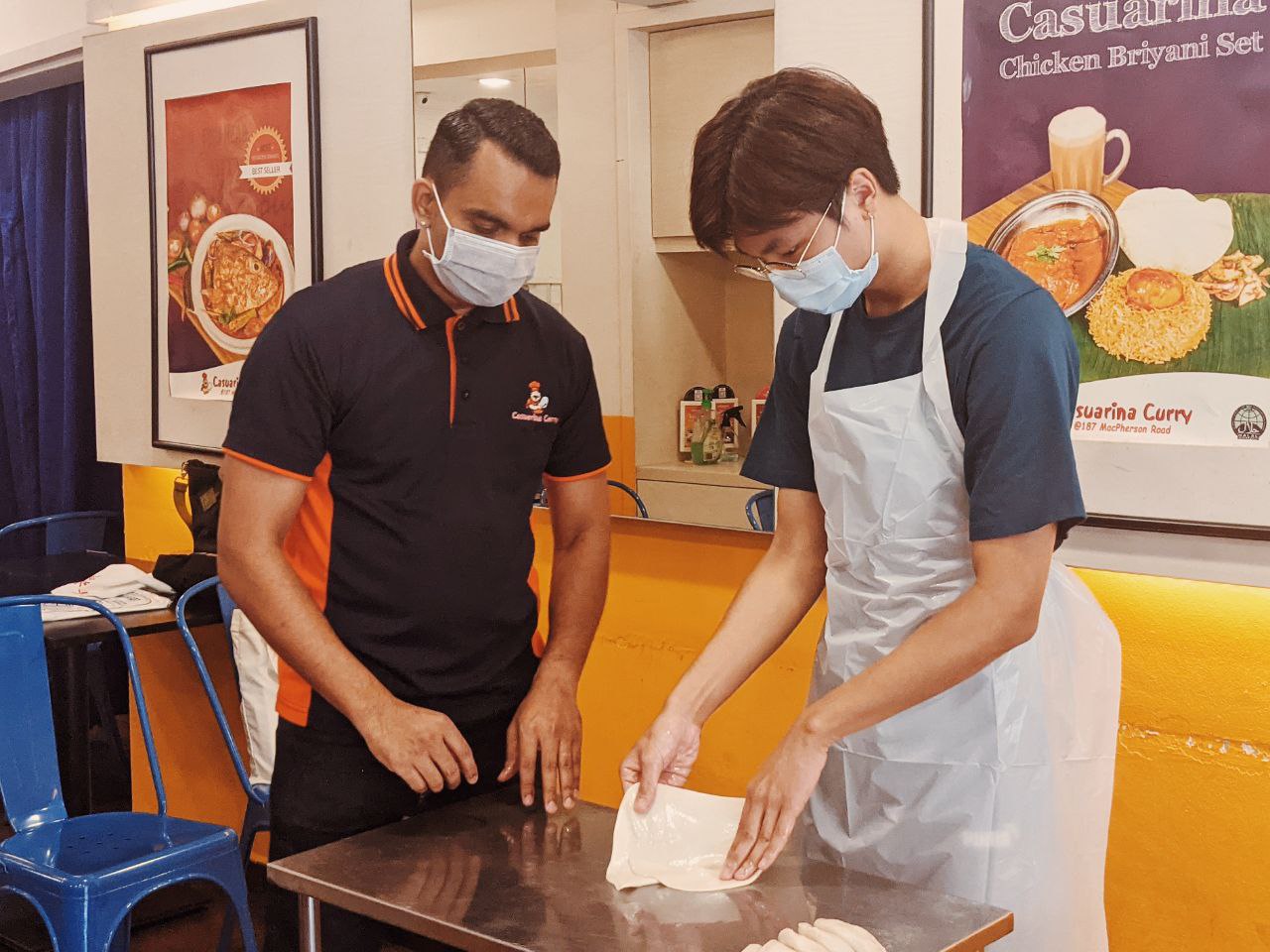 Caleb Cheng, Year 2 Law student learning the ropes of prata-making from an instructor. (Photo courtesy of Debbie Ng) 

