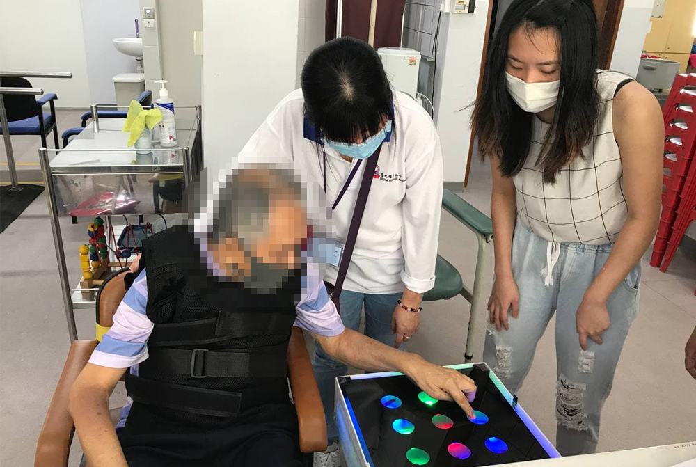 Elderly playing with the prototype under the supervision of a physiotherapist from Metta and NUS student Low Li Ting.

