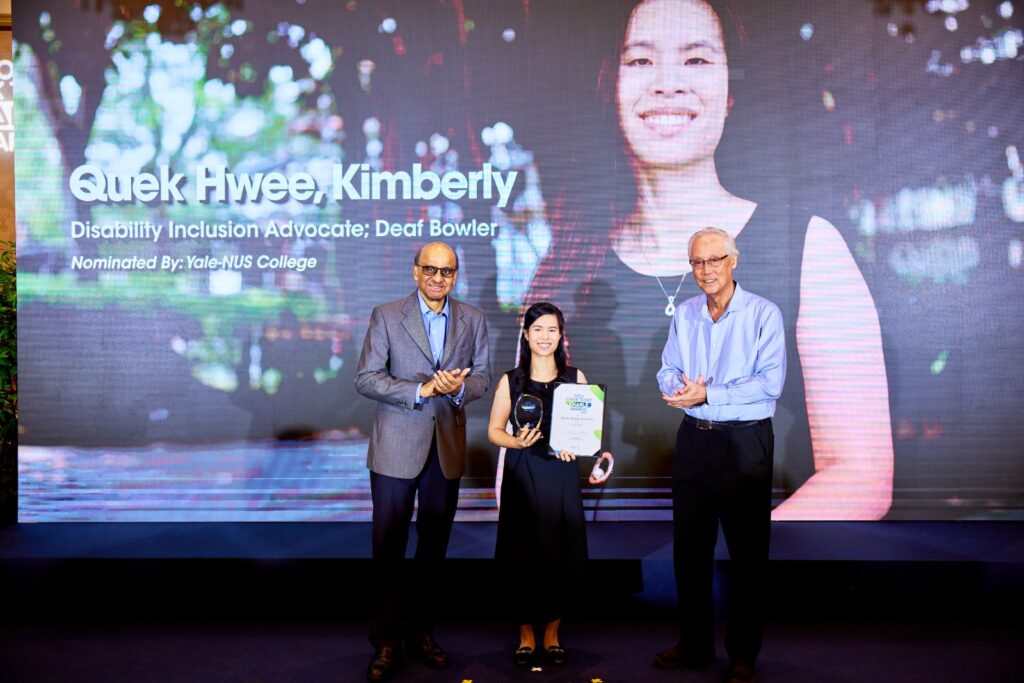 Kimberly Quek standing on stage proudly to receive her award from President Tharman and Emeritus Senior Minister Goh Chok Tong. (Photo: Mediacorp)