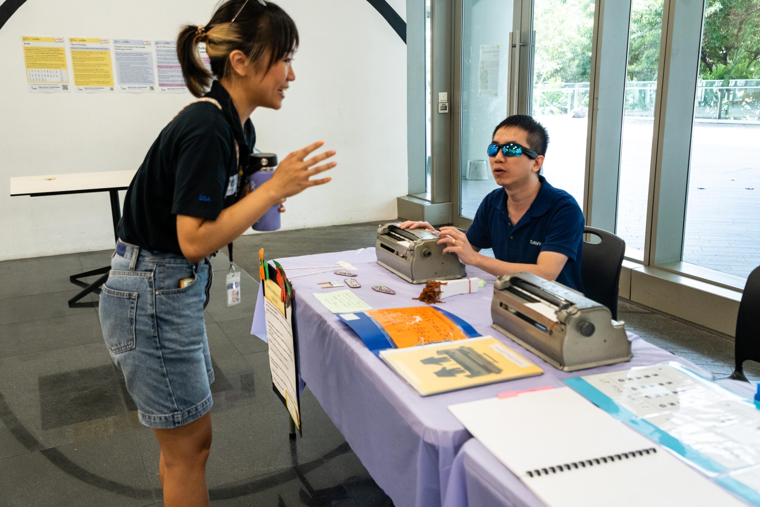 DSC01549 A visually impaired team member from SAVH shows a braille typewriter to an NUS Staff. The staff is listening to the explanation attentively, engaging in the learning.