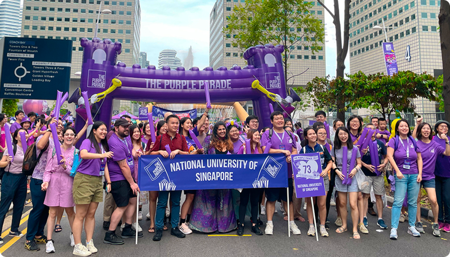 A group of students wearing purple, holding a banner reading "National University of Singapore" at the Purple Parade contingent march