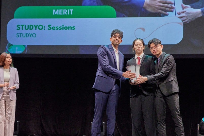Third-year College of Design and Engineering students Low Tse Han (centre) and Kashfy Ilxilim Bin Zulkarna'in (right) accepted the award on behalf of STUDYO from Selvaraj Vijayaragavan, an NAA 2024 Distinction recipient of Community Impact.