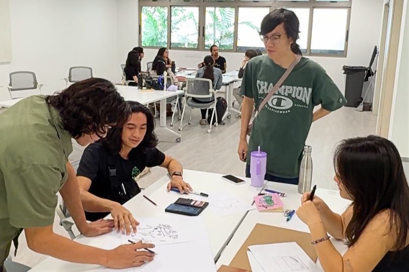 Group huddle around a design sketch on paper.