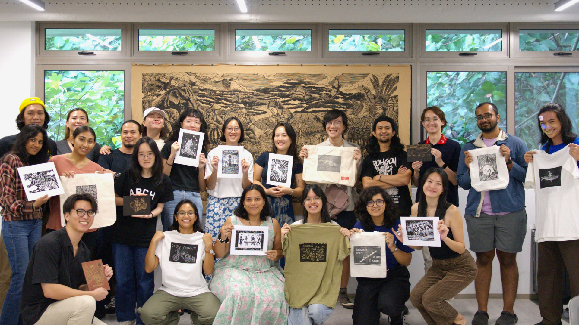 Participants of Workshop for a New Mural @ Yusof Ishak House and instructors from Pangrok Sulap posing with their practice designs and prints on tote bags, paper and T-shirts.