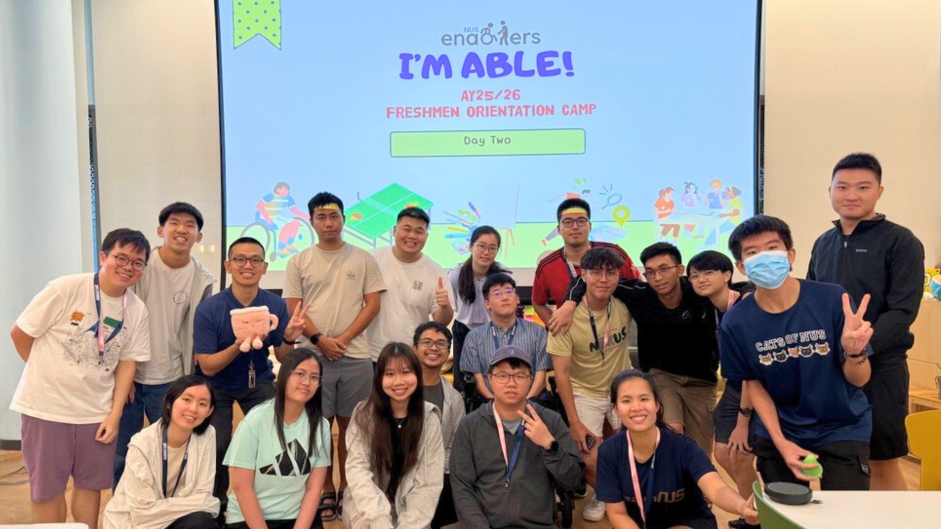 Group of university students posing together in a classroom during a freshmen orientation camp, smiling and making peace signs in front of a projected event slide reading “I’M ABLE! AY25/26 Freshmen Orientation Camp – Day Two.”
