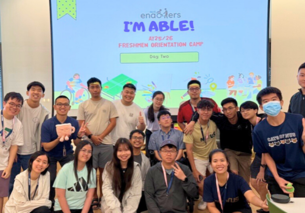 Group of university students posing together in a classroom during a freshmen orientation camp, smiling and making peace signs in front of a projected event slide reading “I’M ABLE! AY25/26 Freshmen Orientation Camp – Day Two.”